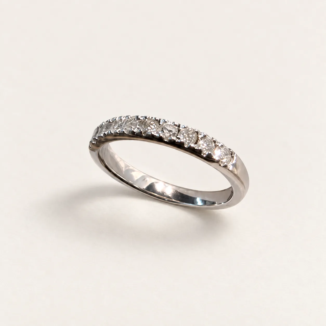 Sonya’s white-gold band with a row of round diamonds, shown at an angle on a warm-white background.
