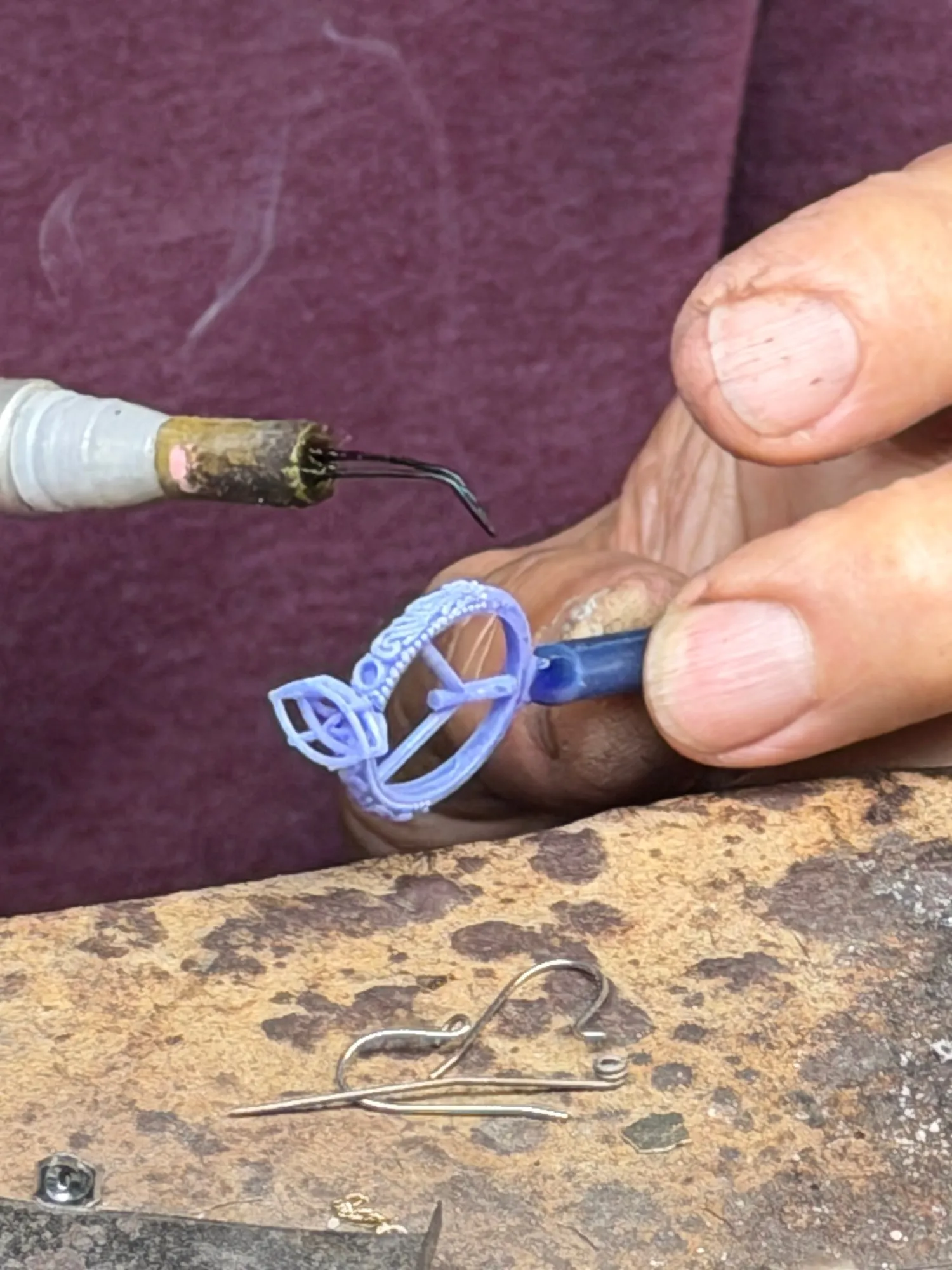The printed model of the ring held at the bench, sprues still attached, being worked with a hot pen before casting.