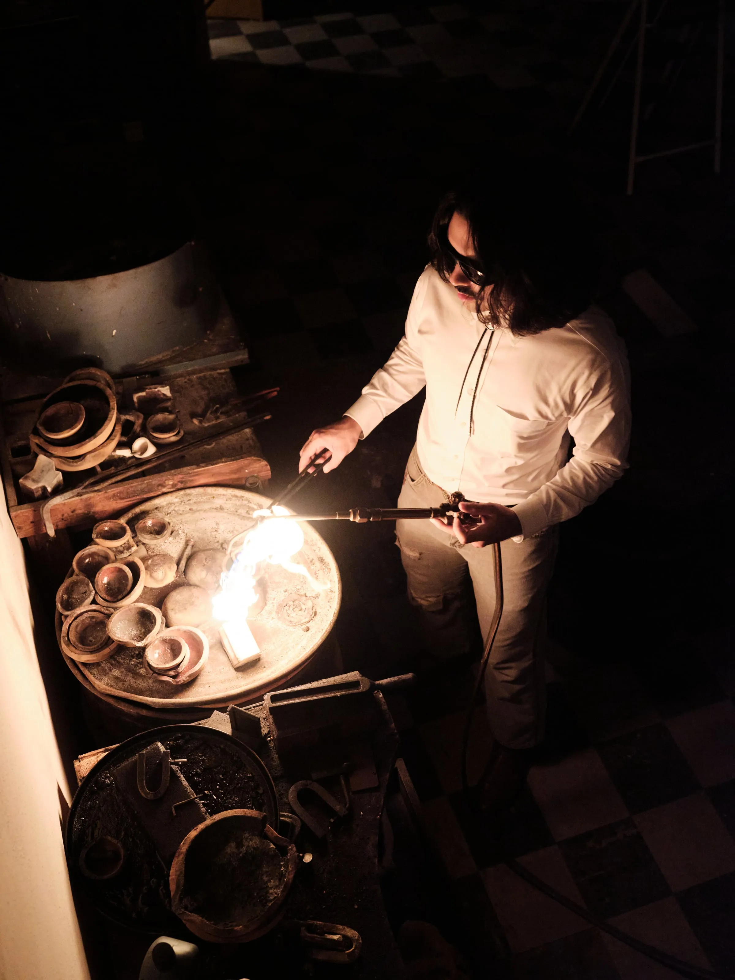 Gabriel working a torch at the bench, molten metal glowing on the soldering pan.